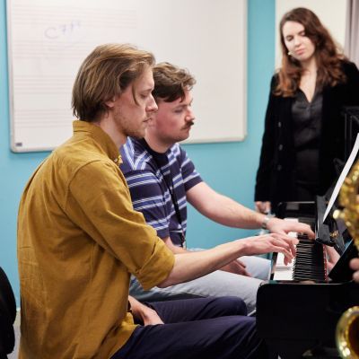 Music Therapy students in a class around a piano, one holding a saxophone